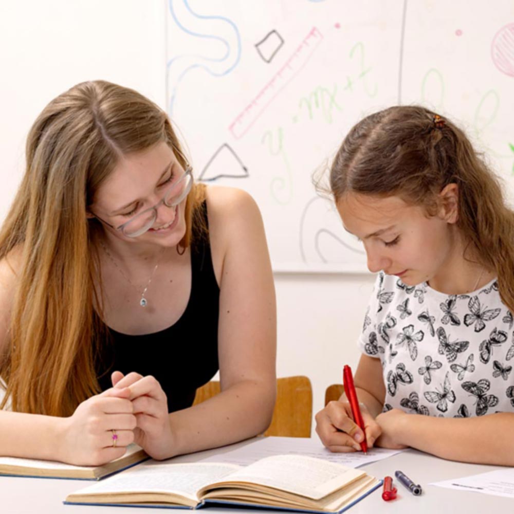 Junge Nachhilfelehrerin hilft einer Schülerin beim Lernen.